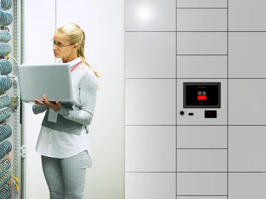 An IT technician working beside a Ricoh smart locker bank fitted with a touchscreen and card reader